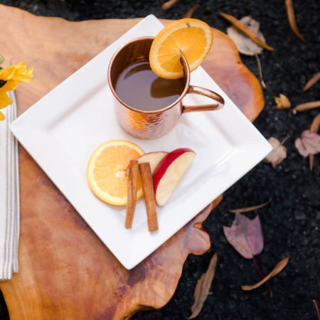 a warm cider drink inside a hammered copper mule mug and is garnished with a slice of orange