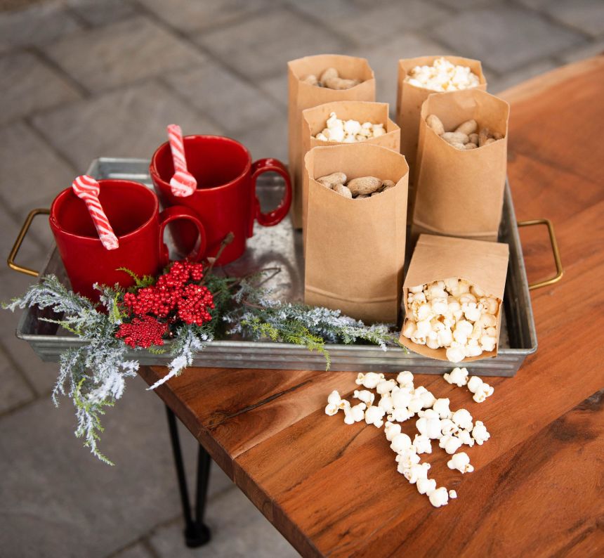 Wooden table sits under a dinner tray filled with bags of popcorn, peanuts and mugs ready for hot cocoa