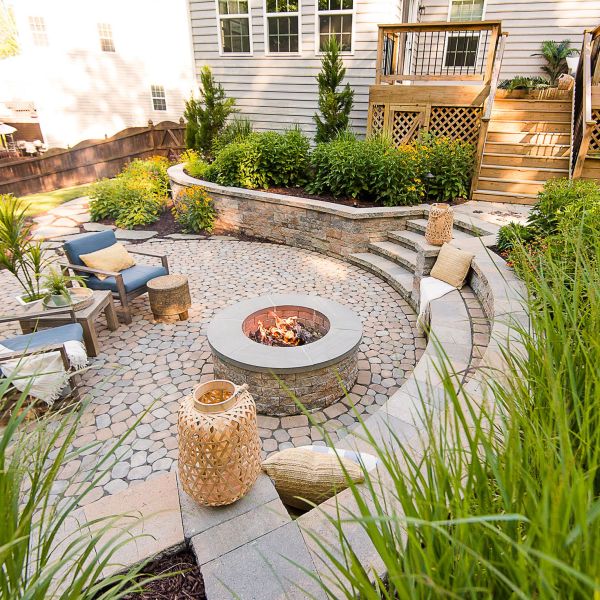 circular paver patio features a retaining wall that functions as a sitting wall beside the fire pit