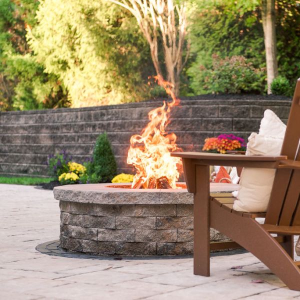 Fire burning in the Stone stacked circular fire pit with adirondack chair and retaining wall