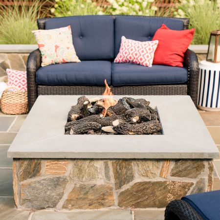 blue outdoor cushions cover the couch and chair that are surrounding the gas-burning fire pit