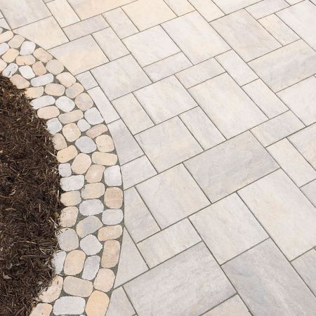large grey stone pavers cover the patio space with a border of smaller more rounded pavers by the mulch