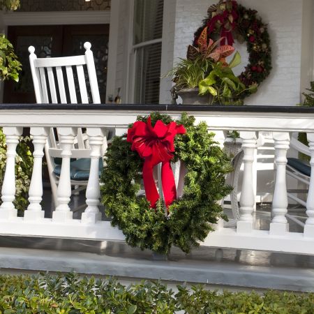 white railing over a stone patio is decorated with a green wreath that has a red bow