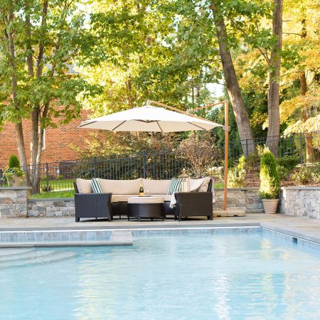 A large dark wicker lounge area is set up beside the pool and covered by an umbrella