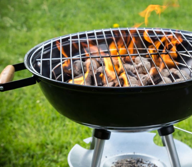 classic black charcoal grill sits in the green grass and is lit and ready to grill