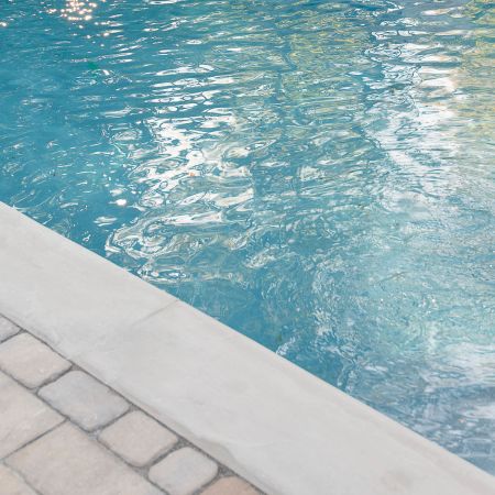 the light grey stone edge  sits above the water rippling in the pool