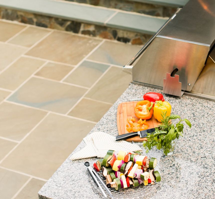 grill island with granite countertop full of veggies and kabobs waiting to be grilled