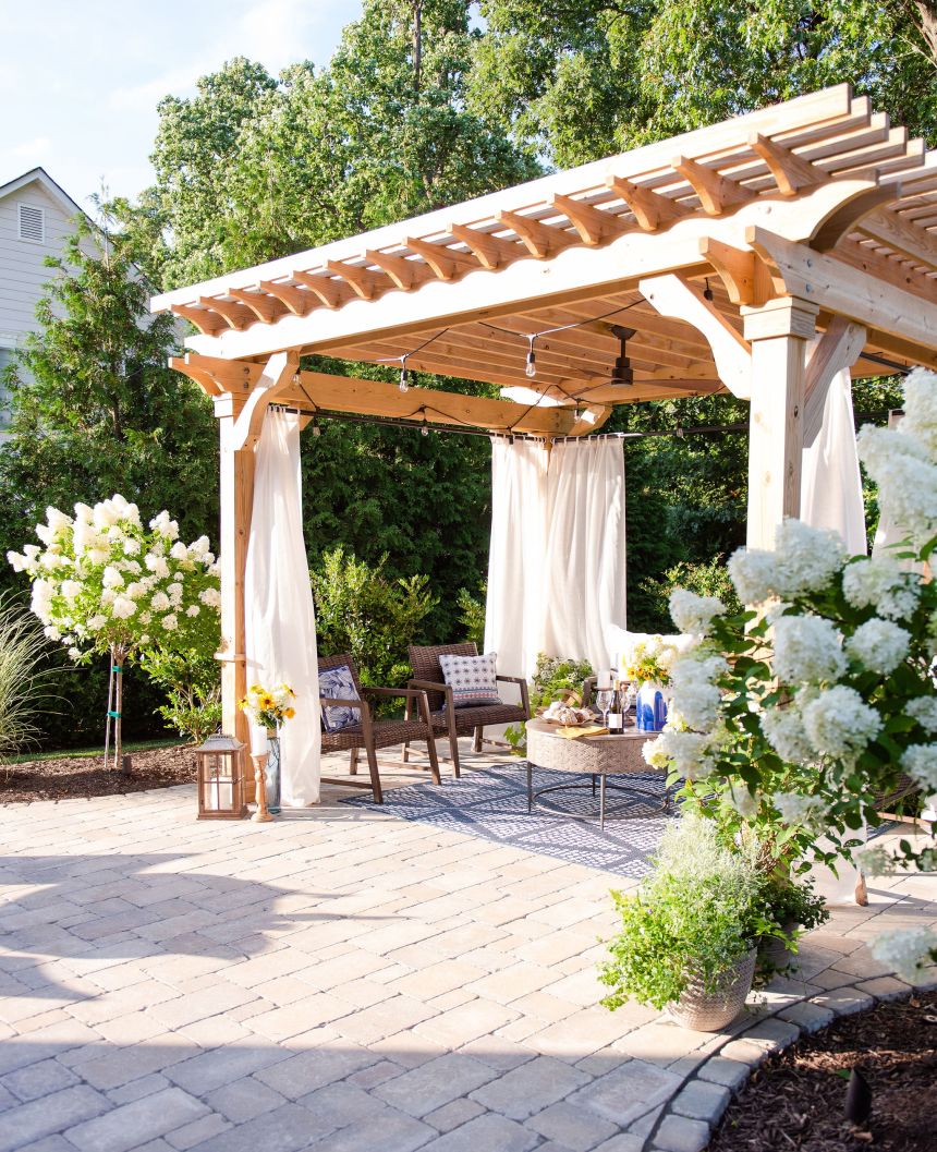 Wood pergola with fan and curtains on a paver patio with hydrangeas