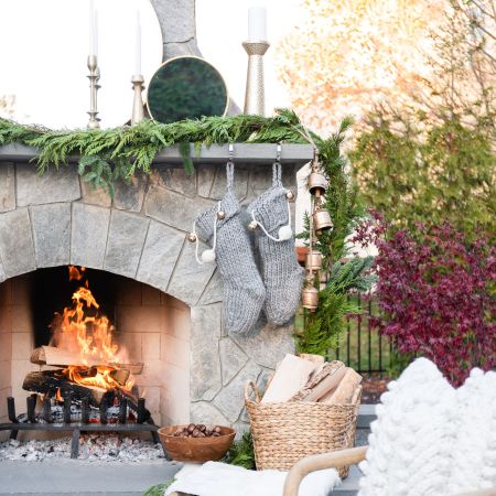 Large stone veneer fireplace is decorated with green garland and a red stocking hanging from the mantle