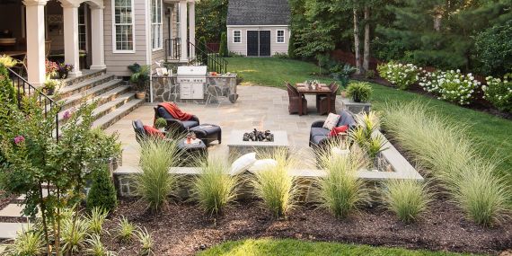 suburban backyard paver patio is surrounded by a perimeter mulched garden before the grass