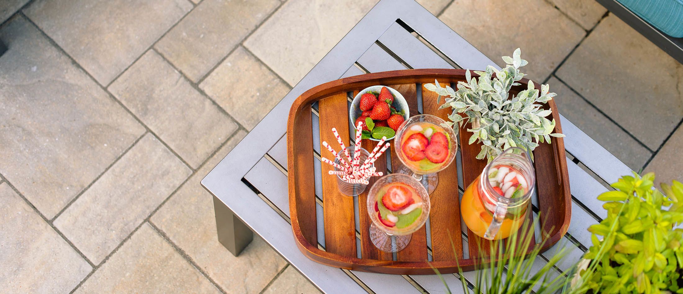 Summer drinks and pitcher are arranged on a drink tray and is on the metal bench that sits on the paver stone patio