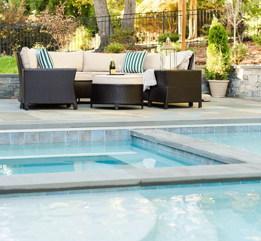 large hot tub installed within one corner of a pool and outdoor seating nearby