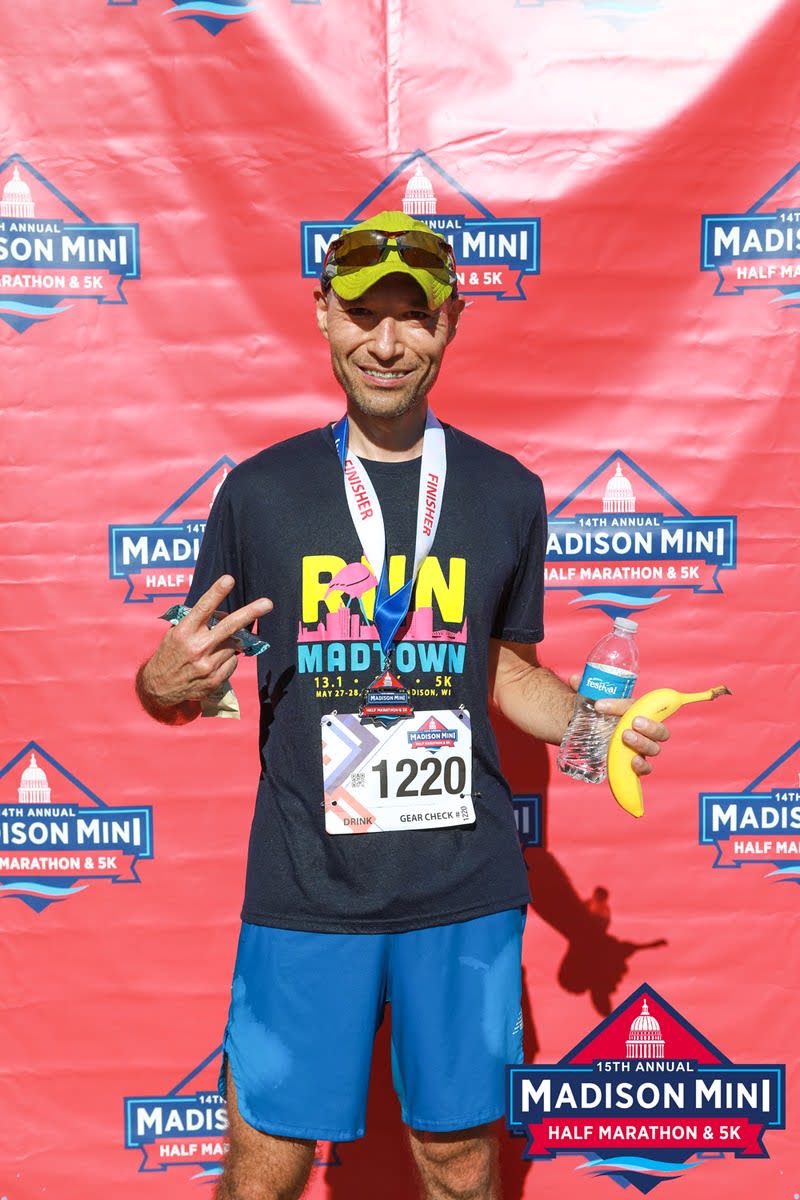 Blog author after running in Madison Mini half marathon getting a finisher portrait taking while holding a banana