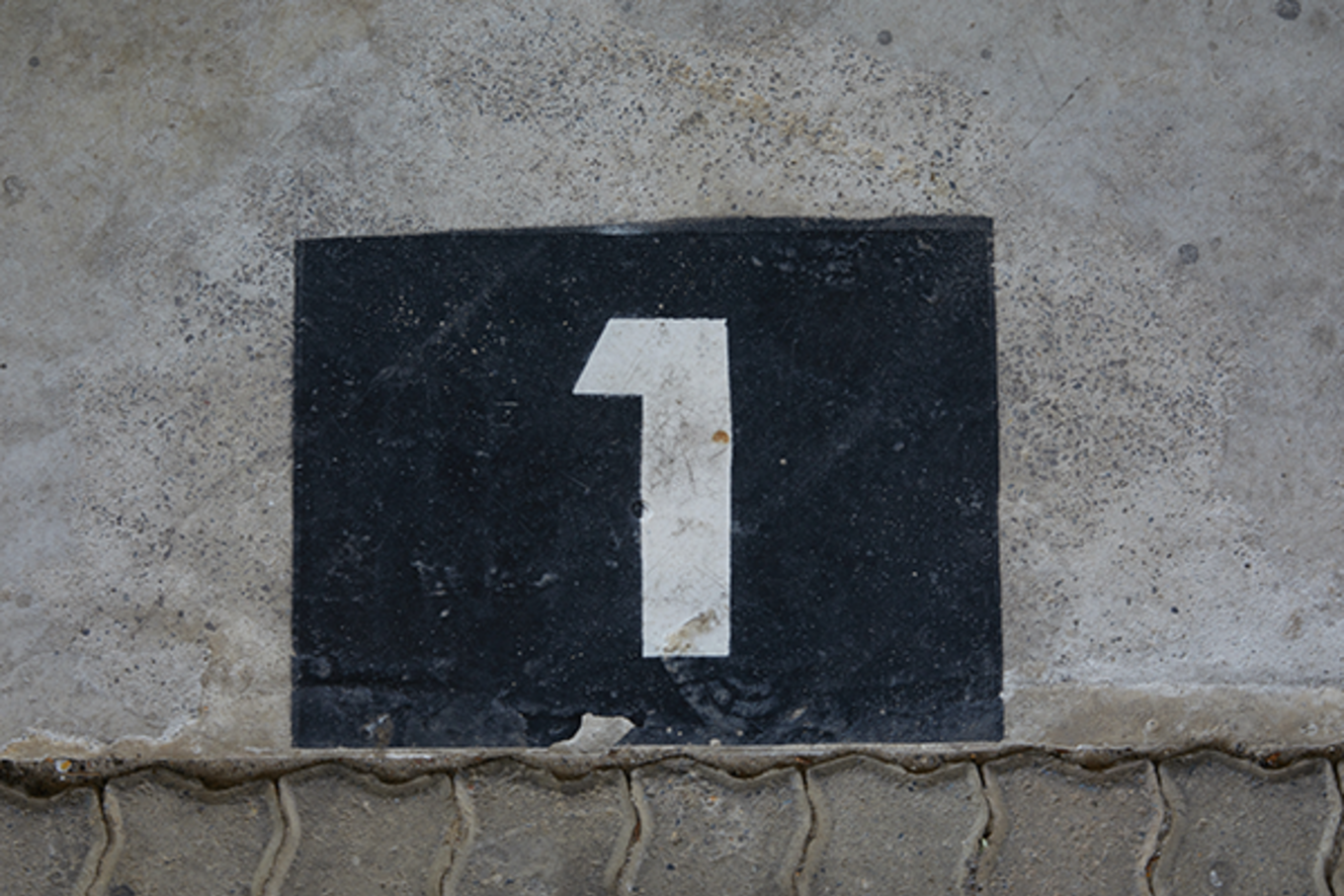 Metal-plated number 1 sign against a concrete background.