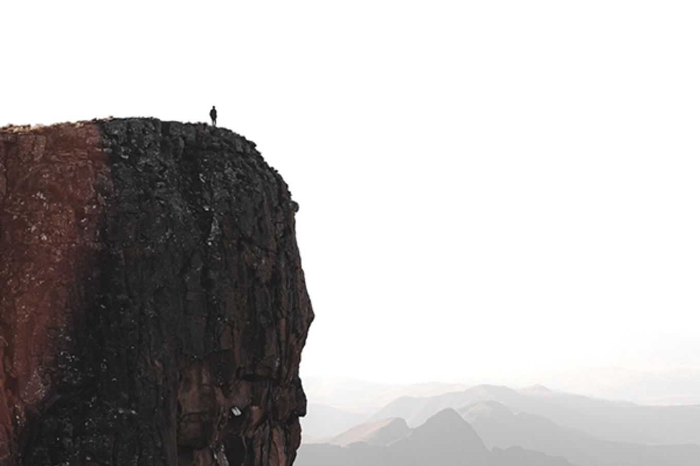 A man stands on the edge of a tall, tall cliff, overlooking the ocean.