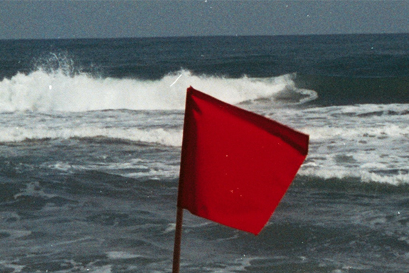 A red flag waves on the beach, which means "dangerous surf."