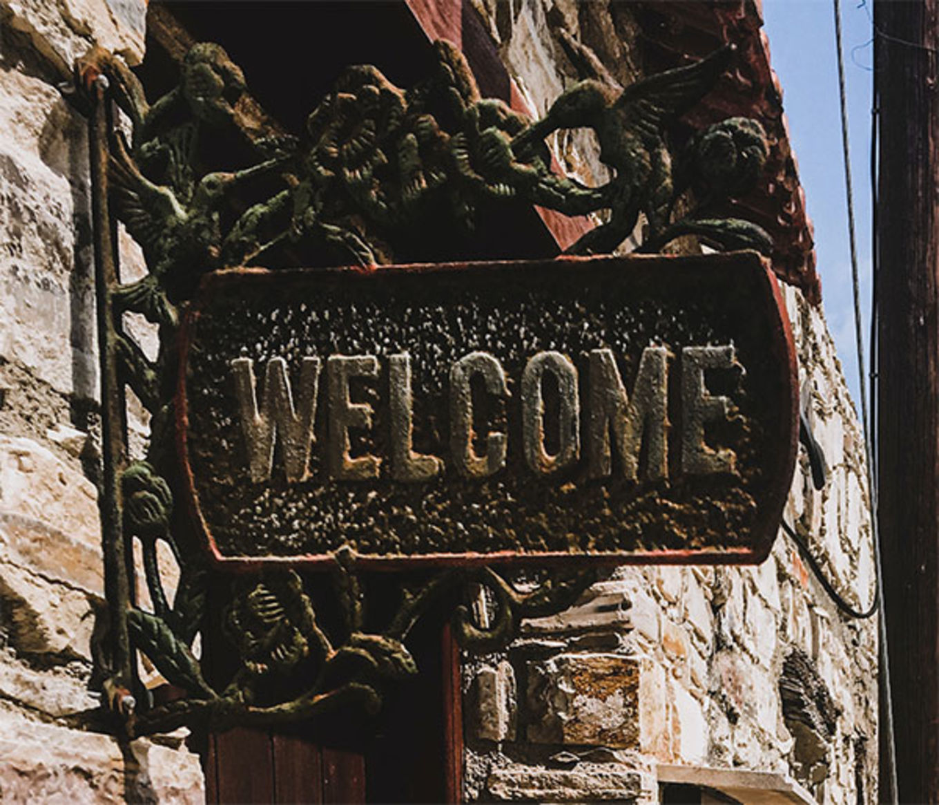 A weathered welcome sign attached to stone and brick building.