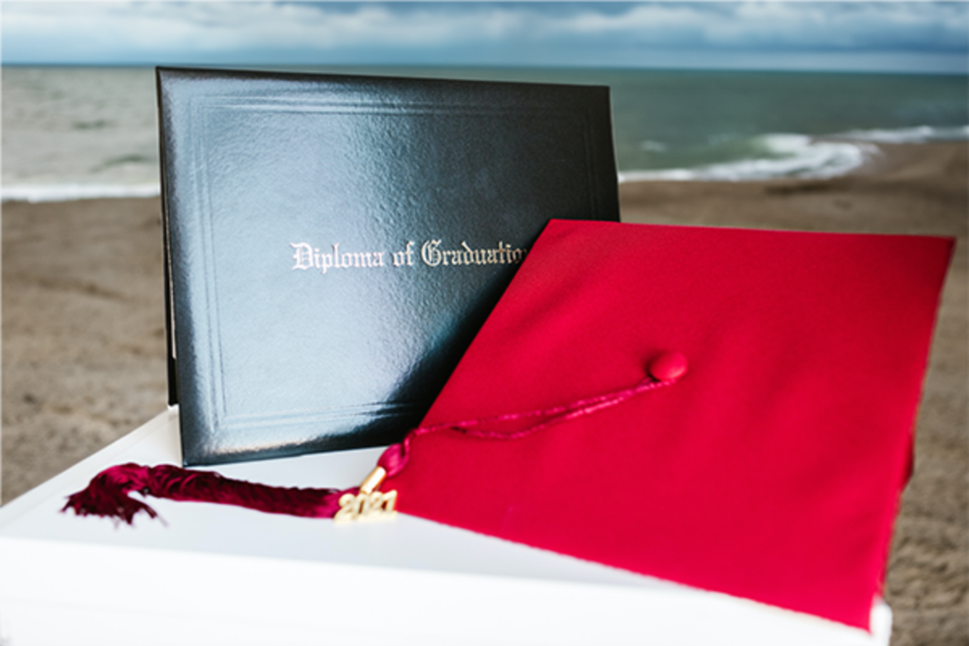 A college diploma on a table that's on a beach with stormy skies overhead.