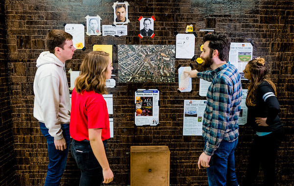 4 people looking at clues on a brick wall at an escape room in Louisville, Kentucky