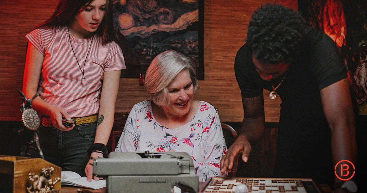 older woman sits at a type writer reading clues held by younger man in a hotel escape room