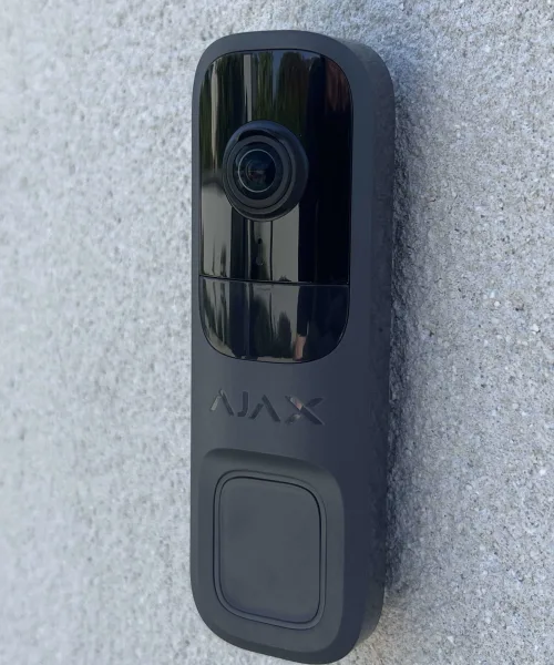 Sonnette vidéo connectée fixée sur un mur crépi, objectif et bouton d'appel