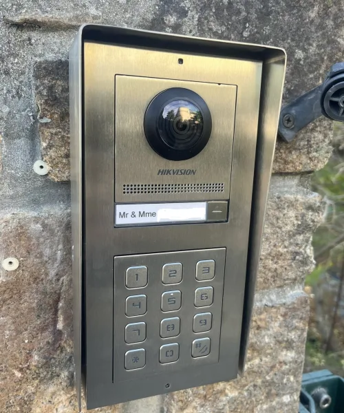 Platine de visiophone connecté à caméra et clavier à code, fixée sur un mur en pierre