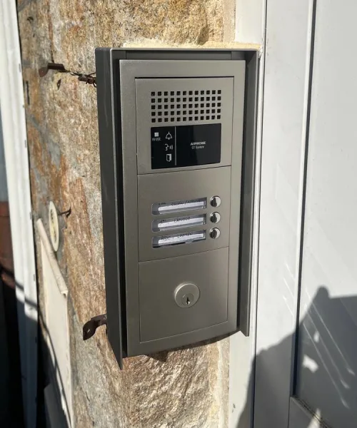 Platine d'interphone audio inox encastrée dans un mur en pierre, haut-parleur et deux boutons d'appel