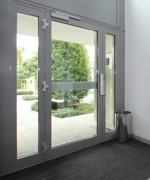Porte vitrée d'entrée d'immeuble à deux vantaux, menuiserie aluminium gris, ouvrant sur un jardin