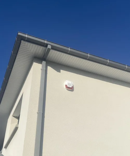 Sirène extérieure fixée en haut d'une façade enduite, sous la gouttière
