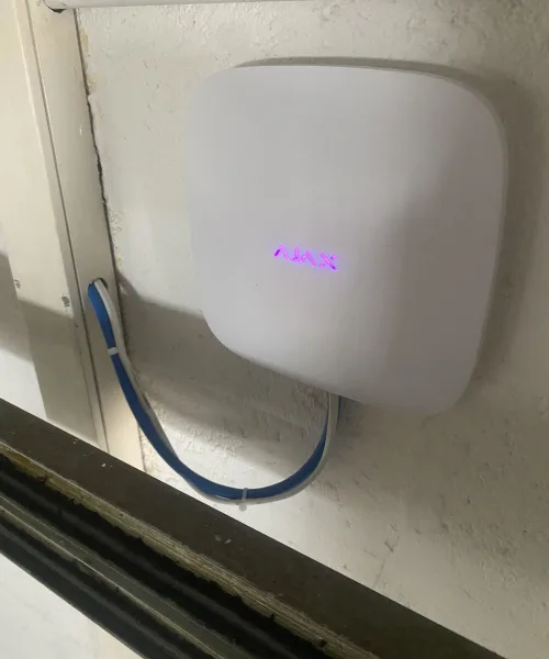 Centrale d'alarme Ajax fixée au mur, voyant violet allumé, câble réseau bleu branché