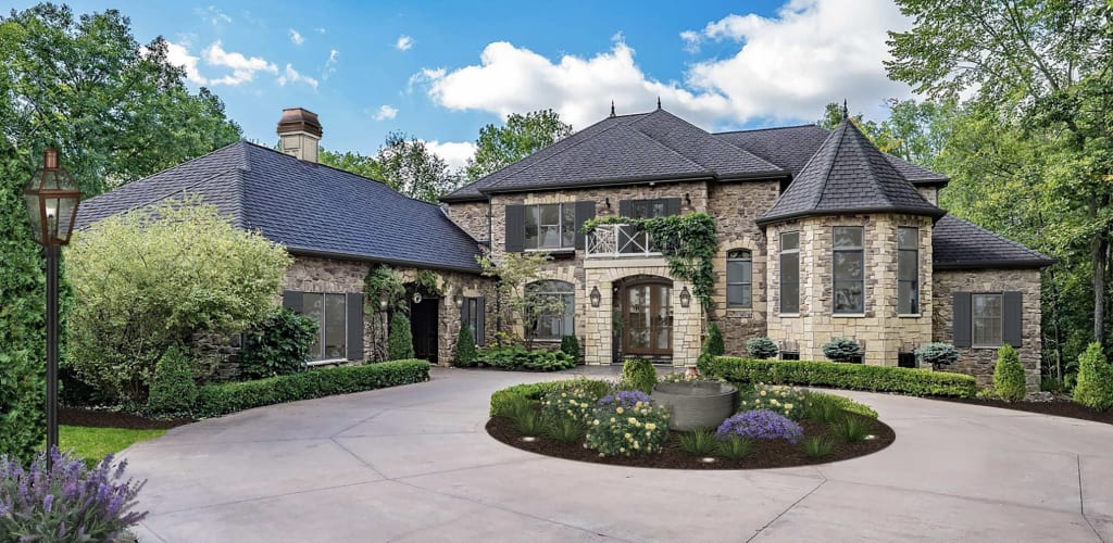 Tudor style home with arched front door, unpainted stone cladding, and a balcony.