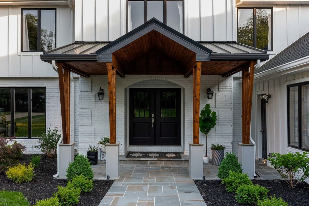 Rustic metal awning with cedar and cement posts over black double front doors