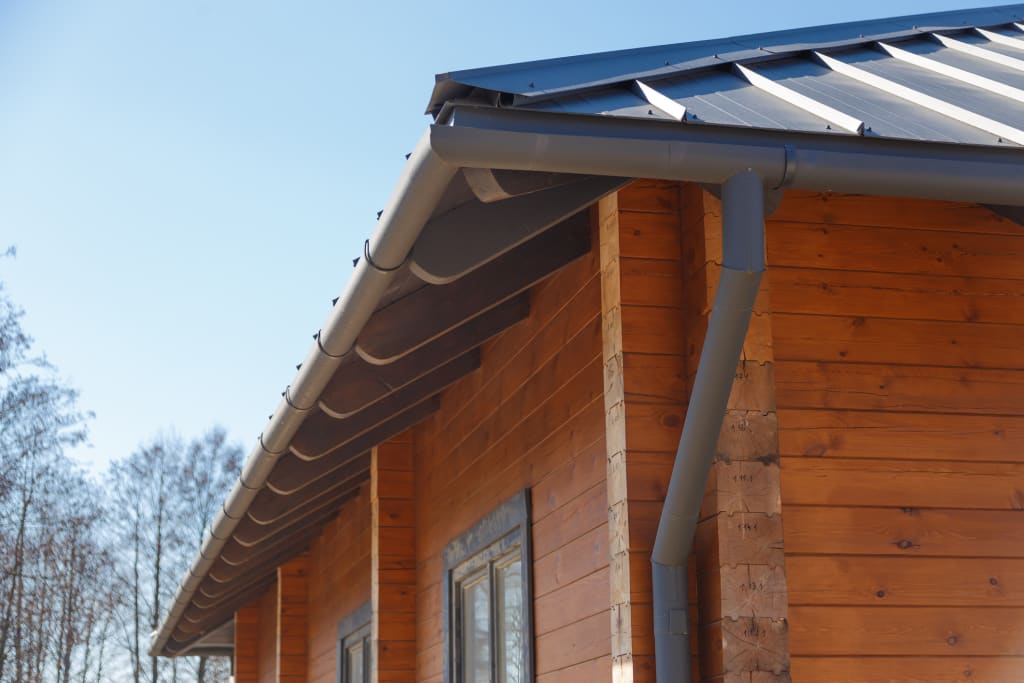 Wood log house with roof drainage gutter system.