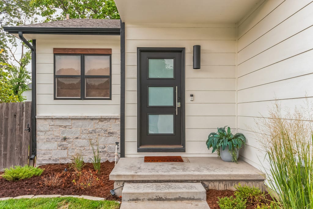 A close-up of the entry area of a home with white siding and stone accents