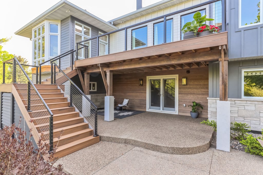 The back of a home exterior with a wooden deck, staircase, and cement patio.