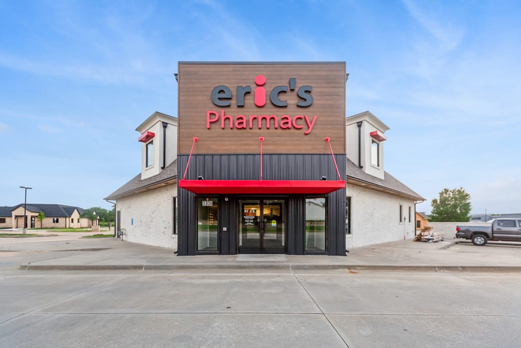 Photo of a pharmacy exterior with wood cladding and a red and black sign.