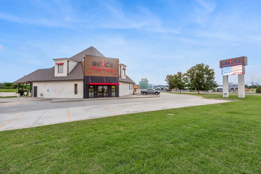 Wide shot of a lime washed pharmacy exterior with a red and black sign