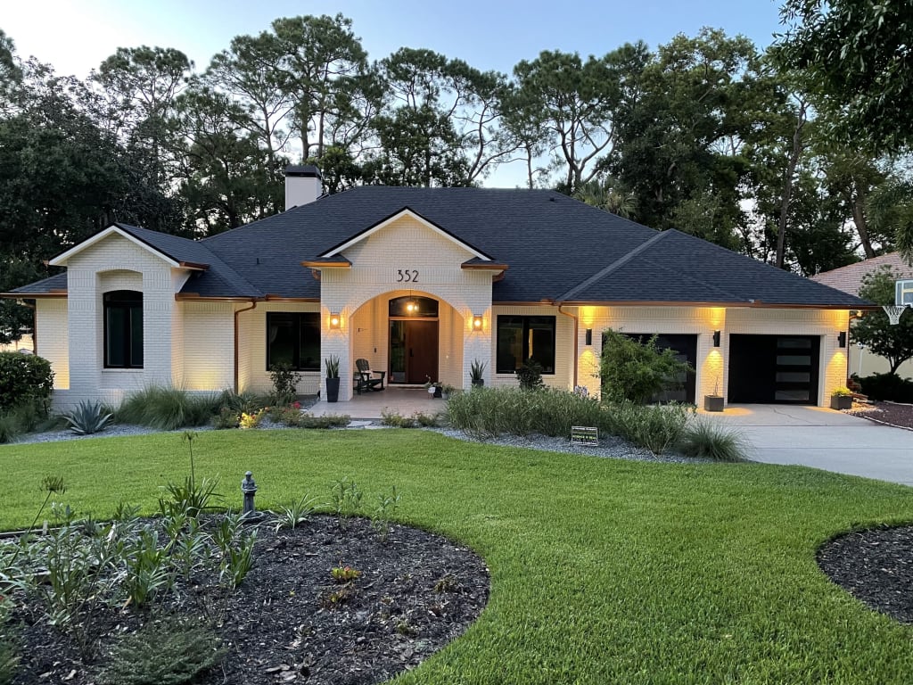 A nighttime photo of a brick home featuring off-white paint