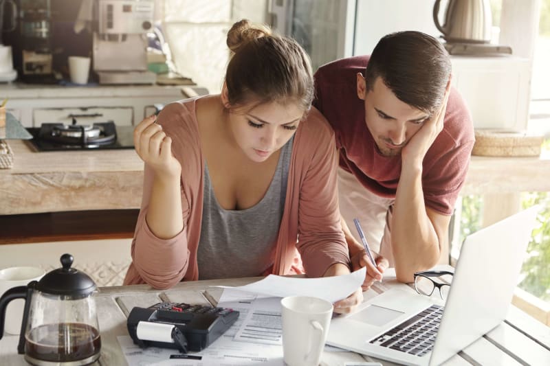 Couple sitting at a kitchen table with a laptop focusing on sorting out their wedding insurance