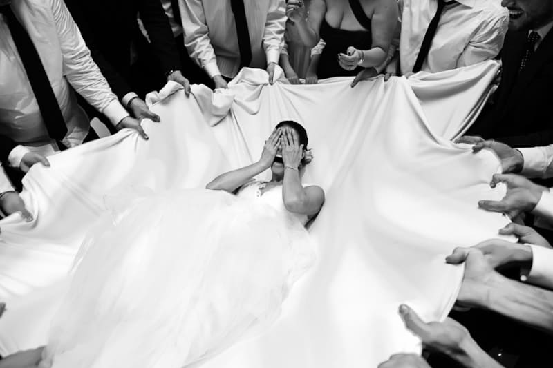 Bridebook.co.uk- bride falling backwards onto white sheet held by guests
