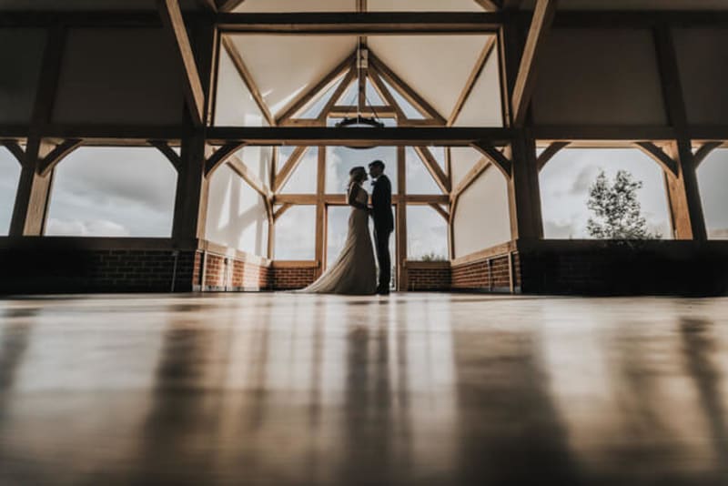 Silhouette of a bride and groom standing under barn beams. 