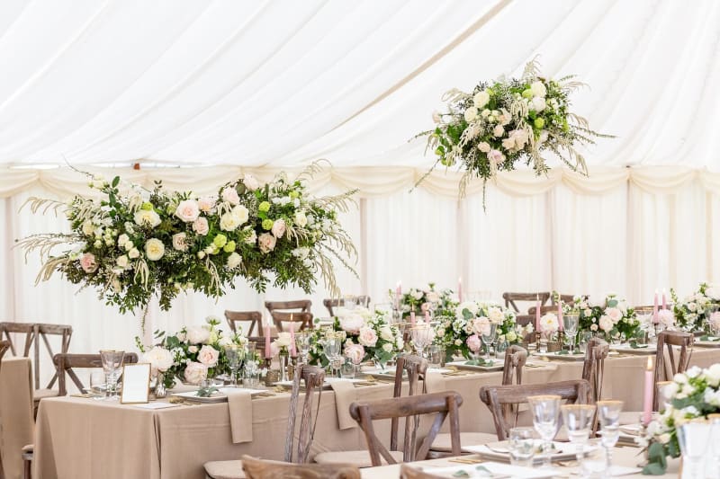 Tables set up and decorated with flowers for a wedding reception under a marquee. 