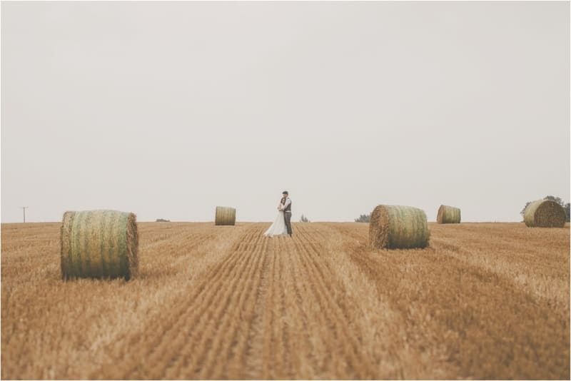 Bridebook.co.uk- bride and groom hugging in a field surrounded by hay bells