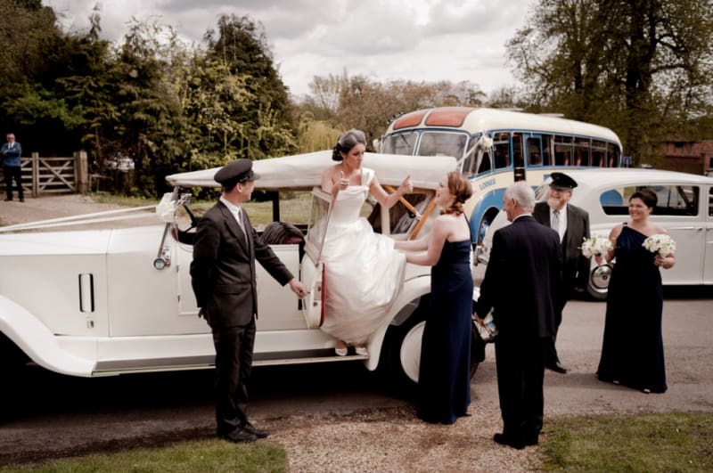 Bridebook.co.uk- bride giving thumbs up to bridal party as she gets out of wedding car