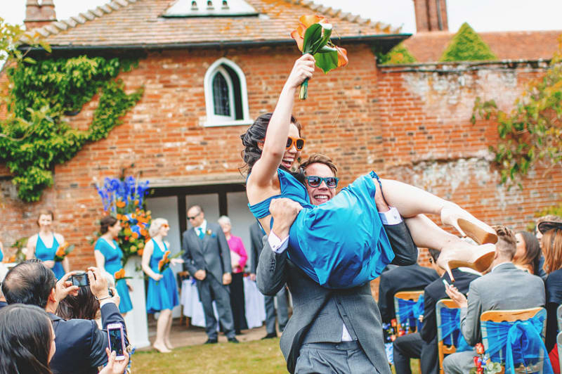 Bridebook.co.uk- usher carrying bridesmaid both wearing sunglasses