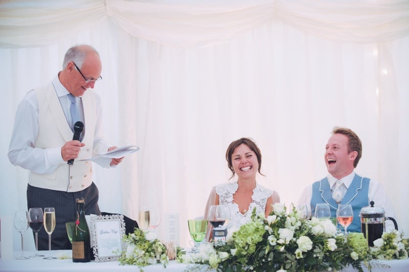 father of the bride reading his speech as bride and groom laugh