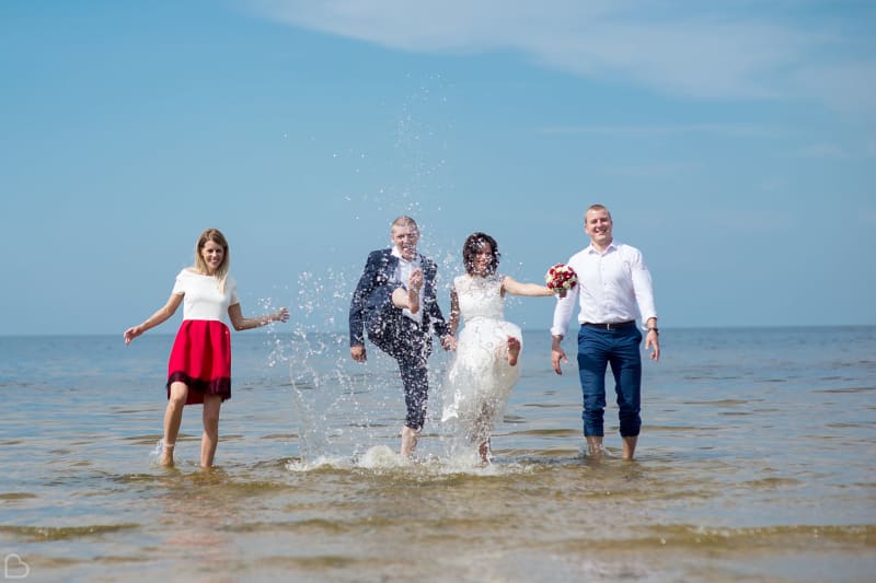 Happy newlyweds and their friends dip their feet in the ocean.