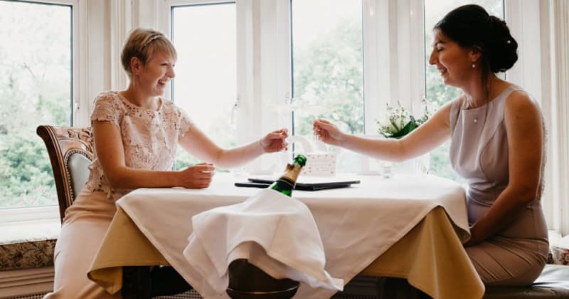 Brides smiling, sitting at table toasting with champagne.