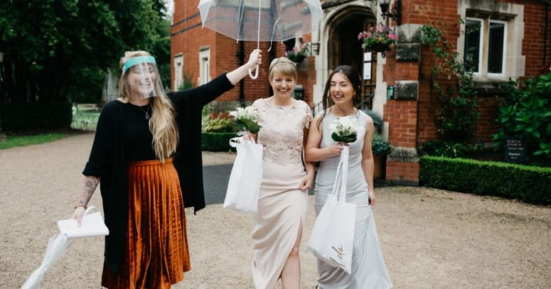 Celebrant and brides standing outside. Celebrant smiling, holding clear umbrella over the happy couple