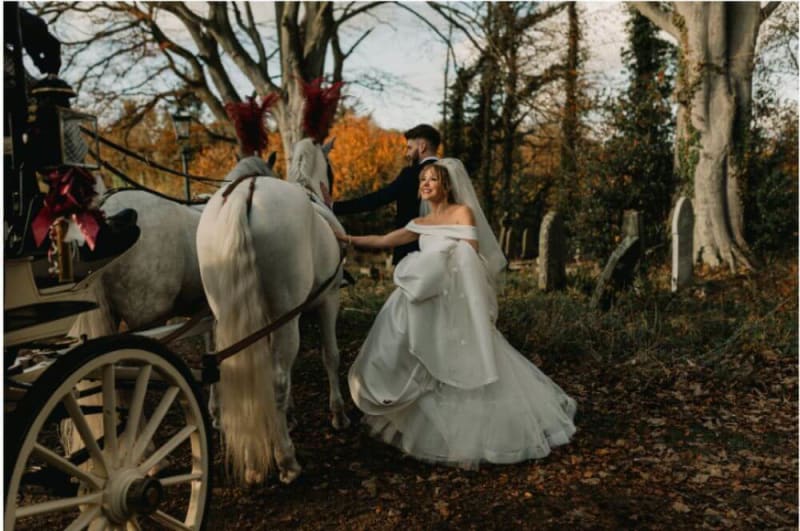 The bride and groom pet one of the horses that pulls the carriage.